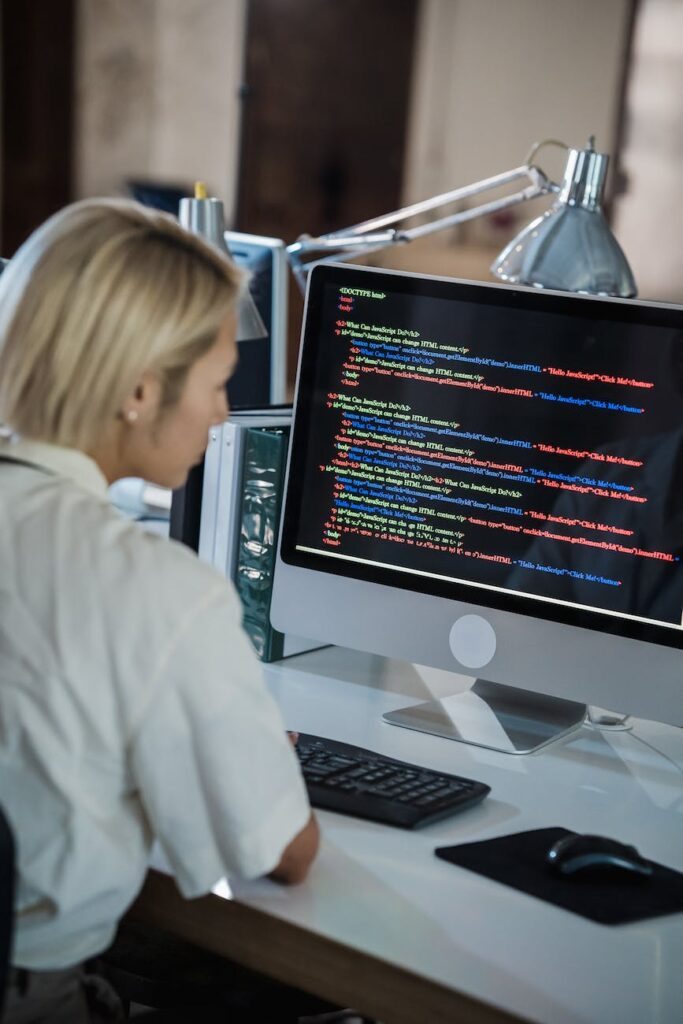woman with blond hair looking at computer screen with multicoloured code