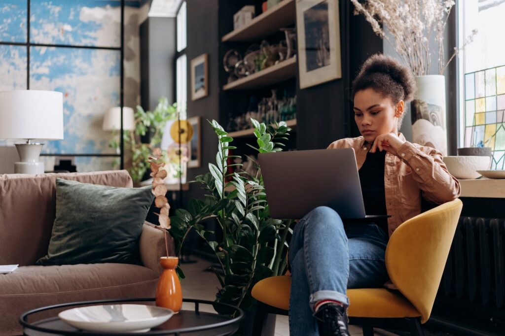 woman in brown jacket sitting on armchair while using her laptop