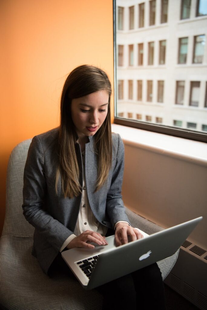photo of woman sitting on chair and typing on silver macbook