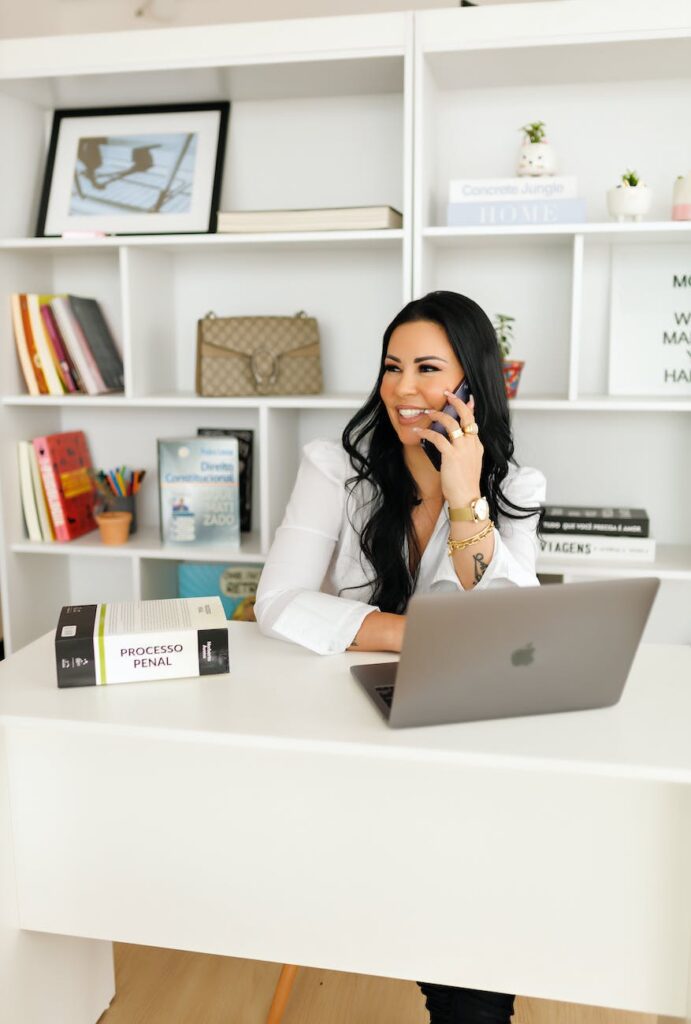 young woman sitting at the desk with a laptop and talking on the phone