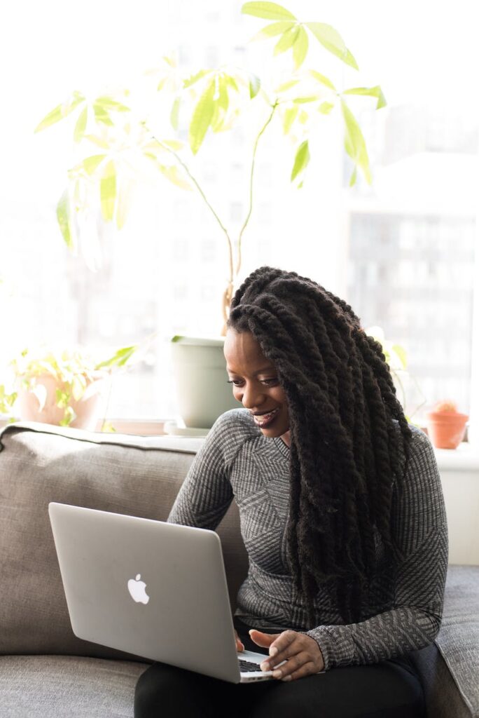 woman sittin on gray couch while holding her apple macbook air