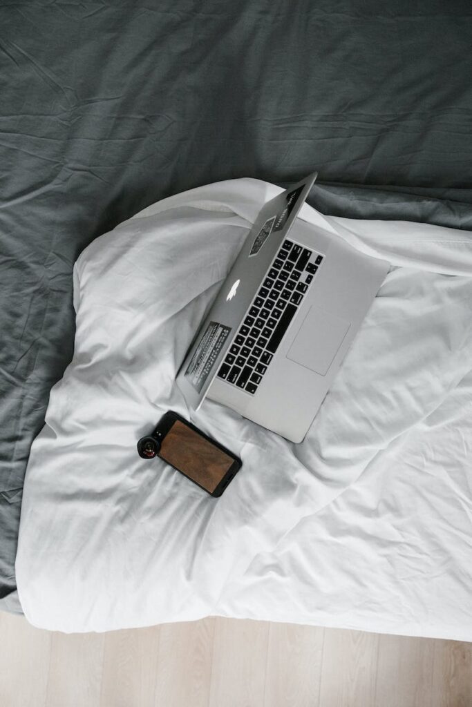 silver macbook pro on white bed blanket