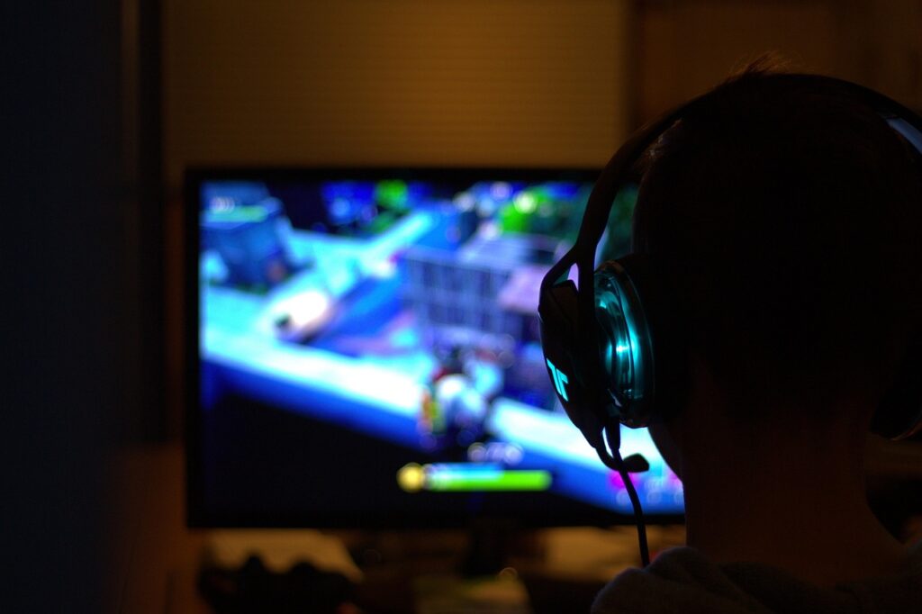A person wearing headphones sits in front of a PC with a game screen open.